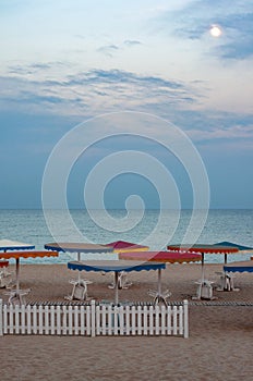 Dusky seascape with colorful beach umbrellas and white wood fence