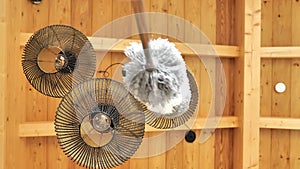 Dust cleaning.Ceiling lights cleaning.fluffy bristle brush cleans metal black lamps under a wooden ceiling. Bottom view.