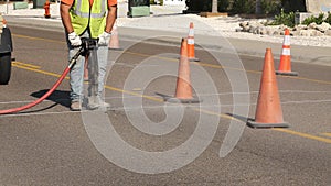 Dust flies from the machine as a man laborer works with a jackhammer on the asphalt of a city street as part of a utility project