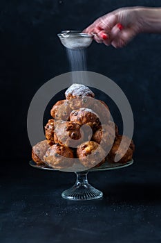 Dusting of icing sugar by a female hand on a stack of oliebollen (translation: Dutch dough fritters
