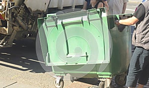 Dustman worker is moving empty garbage container from truck photo