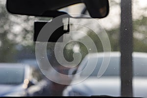 Dusty car windshield seen from a car back seat seeing a modern silhouette CCTV in a foreground and lots of cars from a parking lot