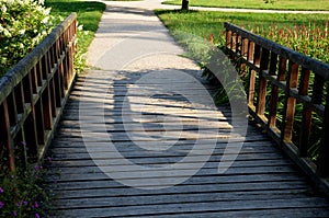 Dusty park path along the pond winding through a meadow. it leads to the bridge and the share of the way are long benches with woo