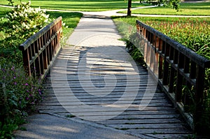 Dusty park path along the pond winding through a meadow. it leads to the bridge and the share of the way are long benches with woo