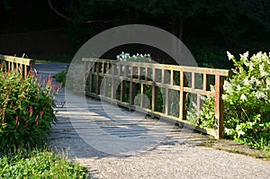 Dusty park path along the pond winding through a meadow. it leads to the bridge and the share of the way are long benches with woo