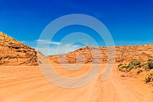 Dusty and unpaved road through the arid and dry desert. Desert with sand dunes and blue sky.