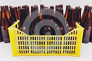 Dusty vintage yellow beer crate with empty brown beer bottles on white background.