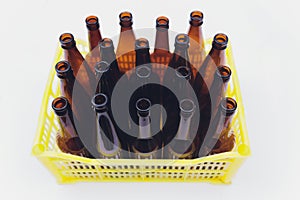 Dusty vintage yellow beer crate with empty brown beer bottles on white background.