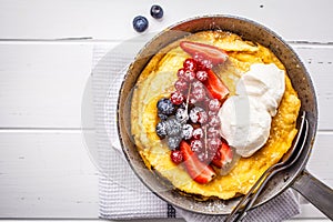 Dutch baby pancake with berries and cream in a cast-iron pan, top view photo