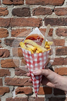 Dutch and Belgian street food, child`s hand with Ð·aper bag of fried potatoes chips with tomatoes ketchup