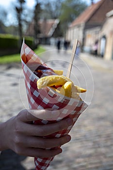 Dutch and Belgian street food, child`s hand with Ð·aper bag of fried potatoes chips with tomatoes ketchup