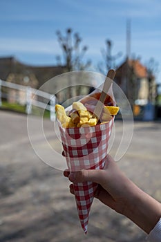 Dutch and Belgian street food, child`s hand with Ð·aper bag of fried potatoes chips with tomatoes ketchup