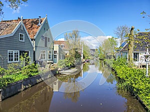 A dutch canal with wooden houses a lush, green countryside with vibrant foliage and rolling hills under a clear blue sky