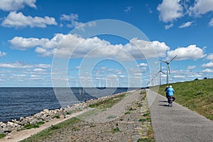 Dutch dike along IJsselmeer with senior cyclists and wind turbines