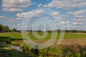 Dutch farm landscape with modern wind turbines  under the blue sky and white clouds
