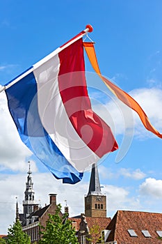 Dutch flag with orange streamer waving in the wind agains a blue sky