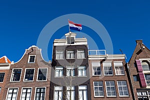 Dutch flags on the canal houses with a blue sky in the center of Amsterdam.