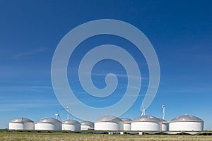 Dutch gas and fuel storage tanks with wind turbines and solar panels in front in the Eemshaven, The Netherlands