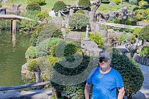 Dutch man standing in blue t-shirt, sunglasses and looking at camera with Japanese garden in background