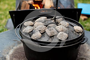 Dutch oven camp cooking with coal briquettes beads on top. Campfire