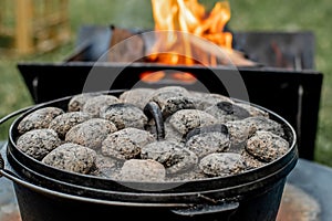 Dutch oven camp cooking with coal briquettes beads on top. Campfire