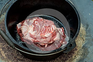 Dutch oven campfire cooking meat. Raw lamb shoulder in the camp oven