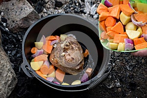 Dutch oven campfire cooking process - lamb and vegetables in a cast iron camp oven