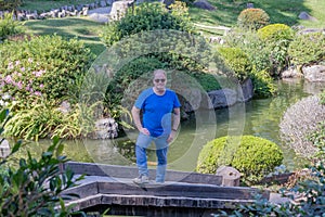 Dutch senior man with sunglasses standing on bridge in Japanese garden