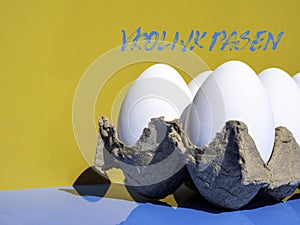 Dutch text Vrolijk Pasen, Happy Easter white eggs in an egg carton outdoor on a sunny day