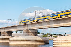 Dutch train crossing the sideskirts of the river Waal in front o