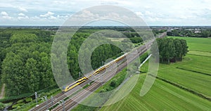 Dutch train passing commuting traveling in forrest grassland nature landscape. Sustainable travel technology by rail
