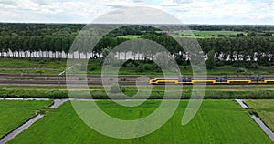 Dutch train passing commuting traveling in forrest grassland nature landscape. Sustainable travel technology by rail