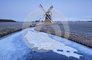 Dutch windmill in dusk by frozen river in winter