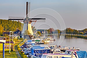 Dutch Windmill In Front of The Canal With Moored Motorboats at Marina Located in Traditional Village in Holland, The Netherlands.