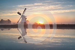 Dutch windmill reflected in river at sunrise