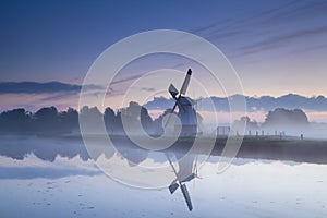 Dutch windmill reflected in river in sunrise fog