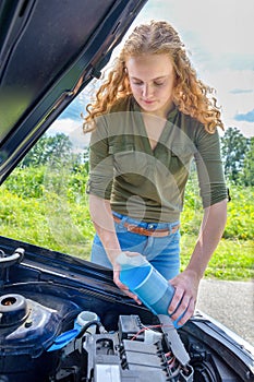 Dutch woman filling car reservoir with fluid in bottle