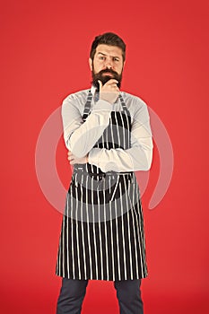 On duty in kitchen. Hipster cafe concept. Man with beard cook hipster apron. Hipster chef cook red background. Bearded