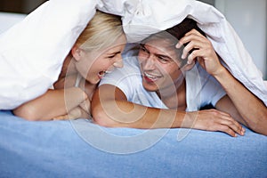 Duvet dalliances. Shot of a happy young couple enjoying a playful moment underneath the duvet.