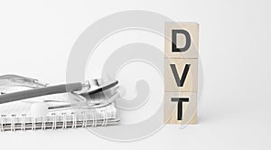 dvt inscription on wooden cubes isolated on white background, medicine concept. Nearby on the table are a stethoscope and pills