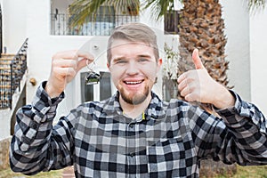 Dwelling, buying home, real estate and ownership concept - handsome man showing his key to new home