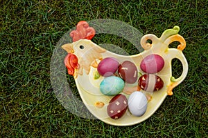 dyed easter eggs on the chicken-shaped plate on green background