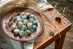 Dyed quail easter eggs in a rustic red brown plate. Easter mood card, copyspace. Beige linen towel, feather, alder cones