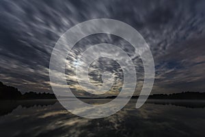 Dynamic clouds in the night over the lake lit by full moon