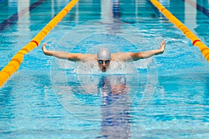 Dynamic and fit swimmer in cap breathing performing the butterfly stroke