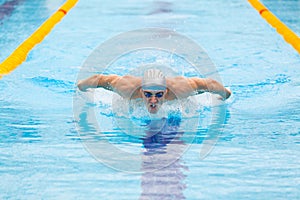 Dynamic and fit swimmer in cap breathing performing the butterfly stroke