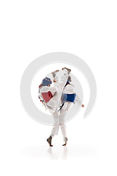 Dynamic image of young girls in helmet and dobok practicing taekwondo stunts, fighting isolated over white background