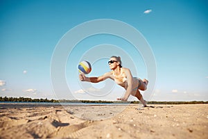 Dynamic image of young woman in motion, playing beach volleyball, hitting ball and falling down on sand