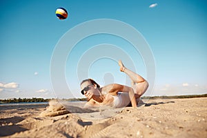 Dynamic image of young woman in motion, playing beach volleyball, hitting ball and falling down on sand