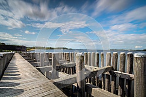 Dynamic moving white clouds against a blue sky above a wooden seahorse near a lake